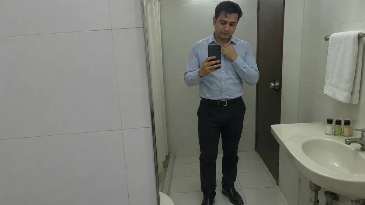 A man taking a mirror selfie in a hotel bathroom in Mumbai while fixing the collar of his blue shirt