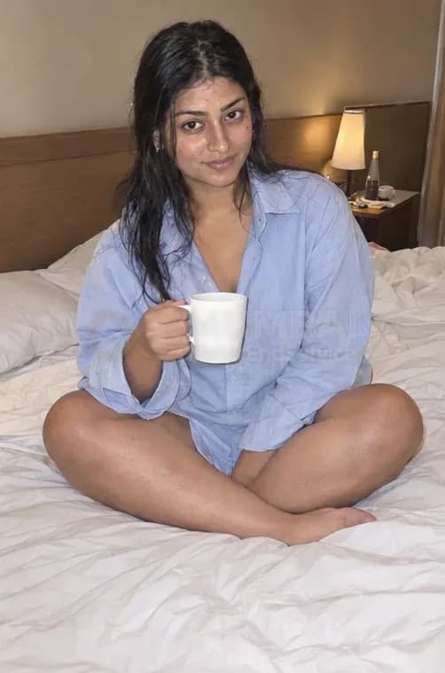 Casual meet escort in a blue shirt sitting on a hotel bed with a cup of coffee