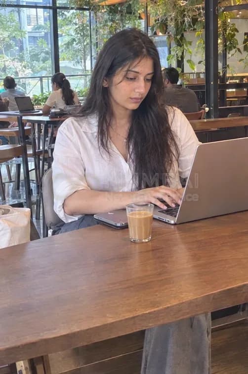 Mumbai escort in a white shirt working on a laptop with cutting chai at a Bandra cafe
