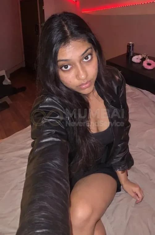 Kinky escort in a black leather jacket taking a selfie on a bed under red lights