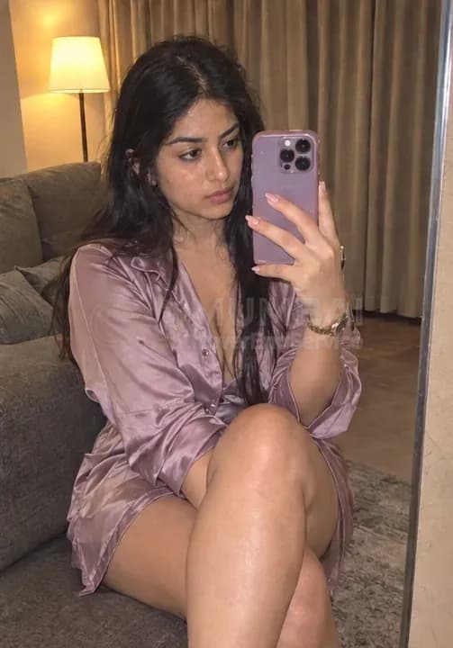 Private escort in a satin shirt dress taking a mirror selfie in her Mumbai flat
