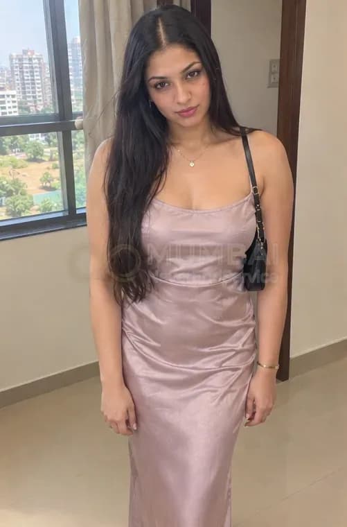 Shemale escort in Mumbai in a pink satin dress standing by the window of her flat