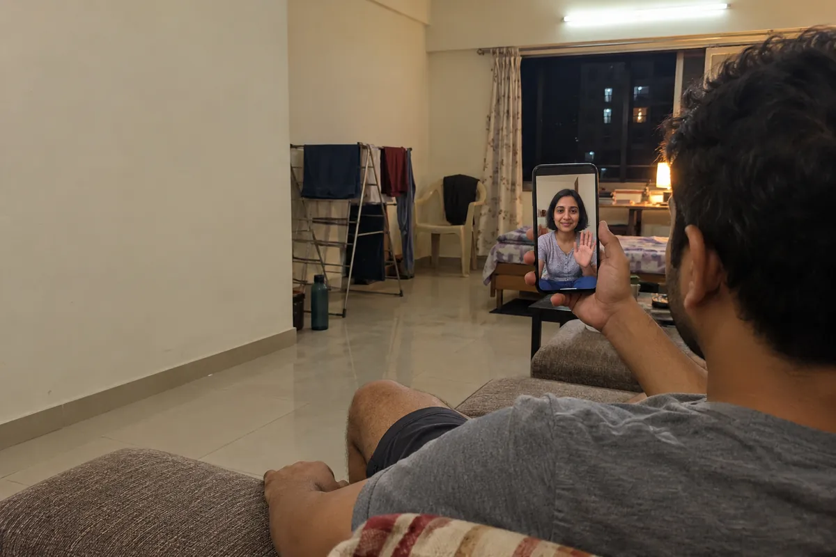 A man on a video call with a woman on his phone, sitting on the sofa of his rented flat in Mumbai
