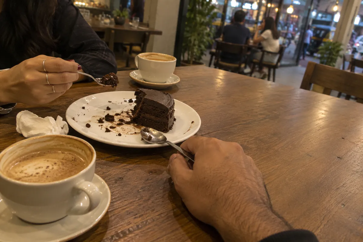 Two people sharing a slice of chocolate cake with coffee at a Mumbai cafe table