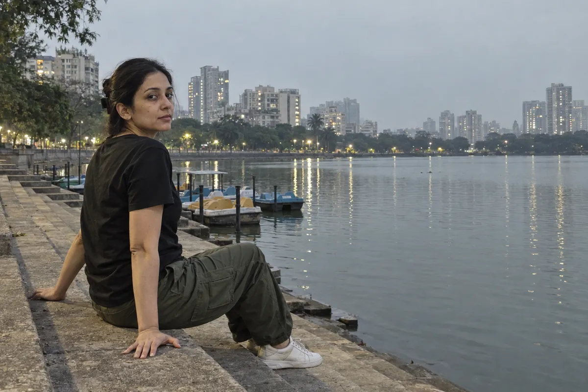 A woman in her thirties in a black t-shirt, hair clipped back, sitting on the steps of Masunda lake in Thane in the evening