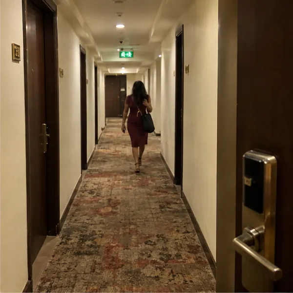 A call girl in a maroon dress in a Mumbai hotel corridor, checking the room number on her phone